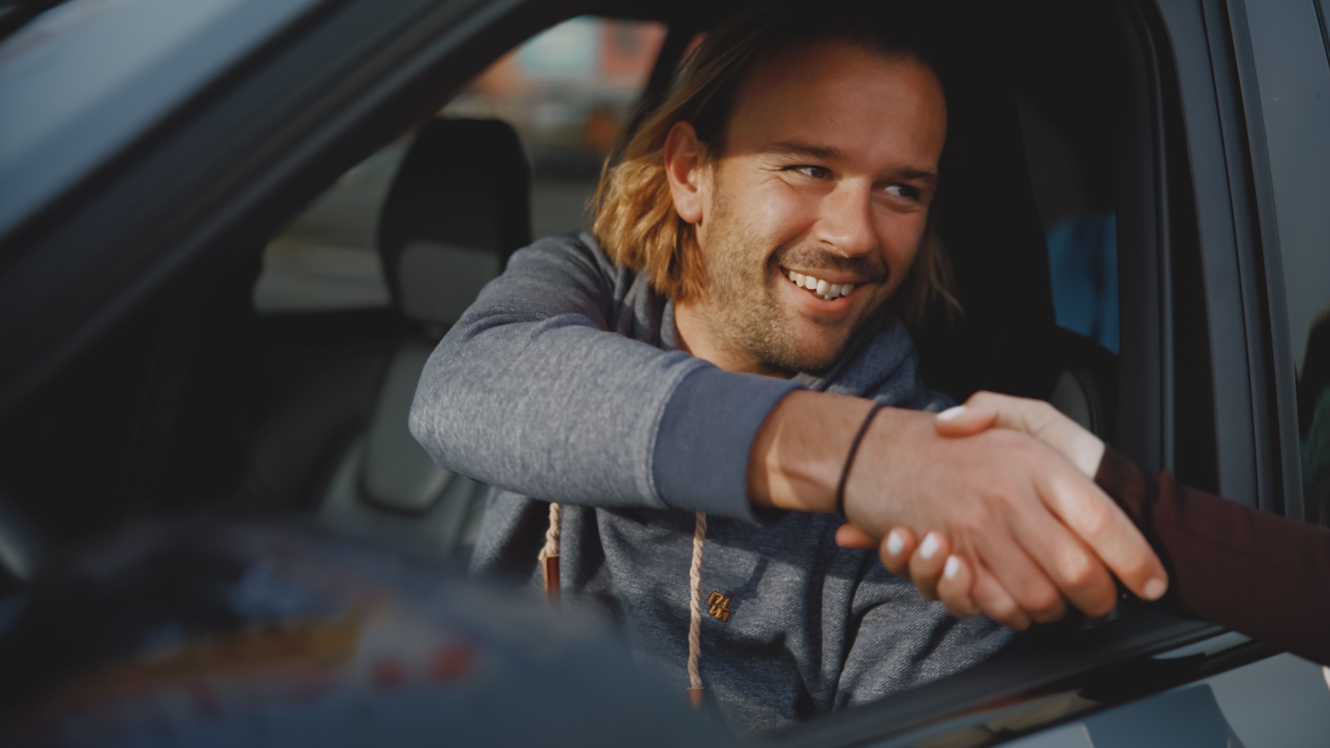 Smiling man sitting in new car and shaking hands with salesperson at dealership